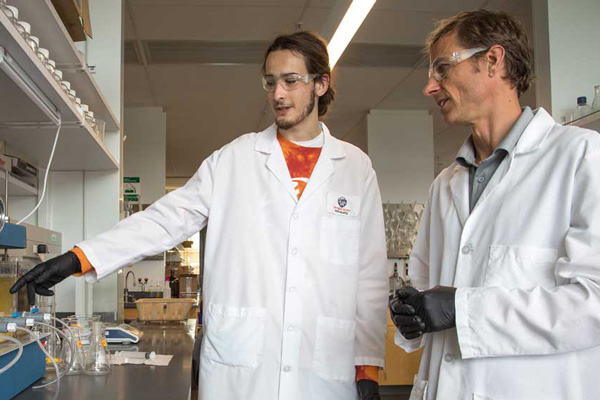 Lab space with two men in white coats, a student pointing on the left and Jeff Nason on the right